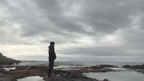 a man looks out at an overcast beach on a grey cloud day