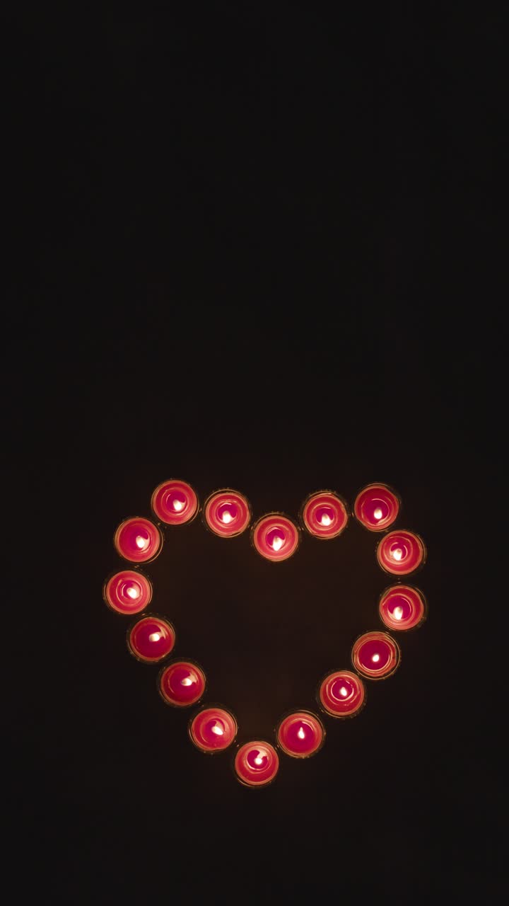 video vertical de las velas rojas encendidas en forma de corazón romántico que se apagan sobre un fondo negro
