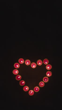 Vertical-Video-Overhead-Shot-Of-Lit-Red-Candles-In-Shape-Of-Romantic-Heart-Being-Blown-Out-On-Black-Background