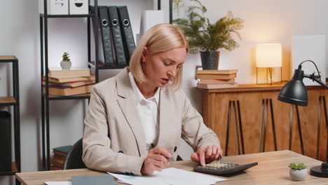 upset mature businesswoman using calculator feeling worried about financial problem at office desk