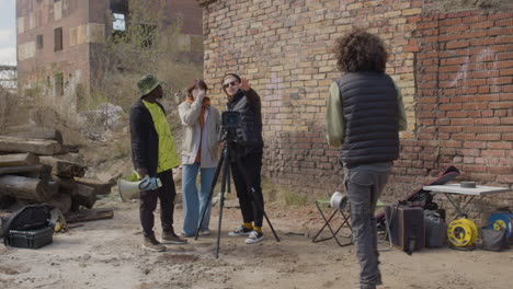 tres compañeros de producción hablando de un proyecto de grabación frente a una cámara en un trípode en la calle mientras otro trabajador toma notas