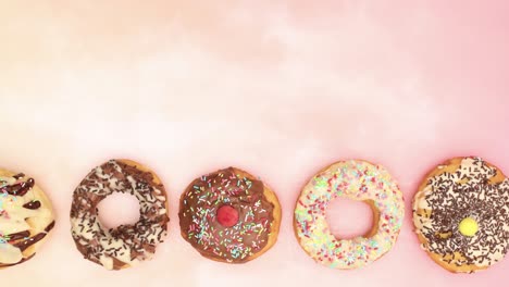 delicious donuts decorated with chocolate passing on bottom of pink background - stop motion