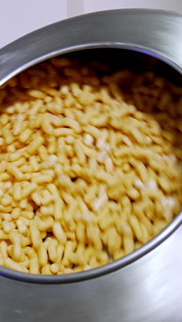 metal tank rotating and mixing the corn snacks inside. thick maize sticks are covered with sugar glazing. food factory production. vertical video
