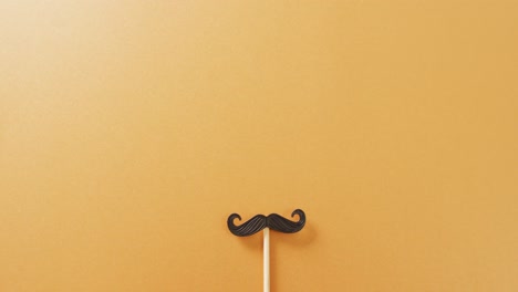 Video-of-false-moustache-on-stick-on-yellow-background-with-copy-space