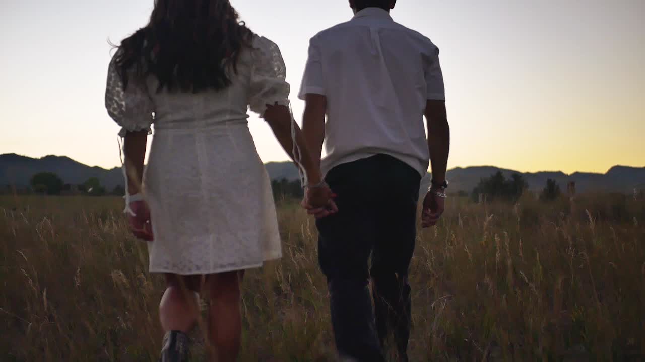Boy and girl hold hands and walk in a field in slow motion during sunset