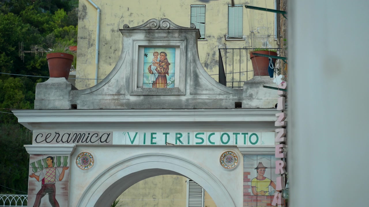 L'ingresso ad arco di Ceramica Vietriscotto riempie l'inquadratura con figure di lavoratori dipinte e un pannello centrale in piastrelle a tema religioso