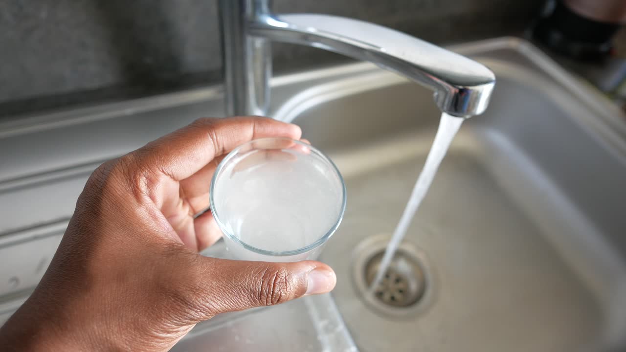 persona llenando un vaso de agua de un grifo del fregadero de la cocina
