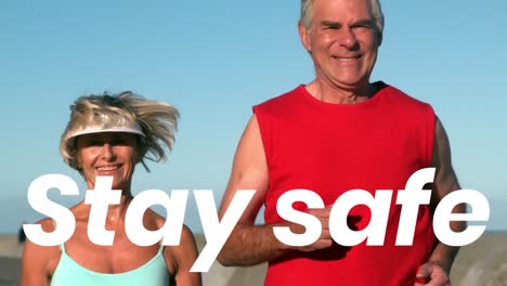 Animation-of-stay-safe-text-over-senior-couple-running-on-beach