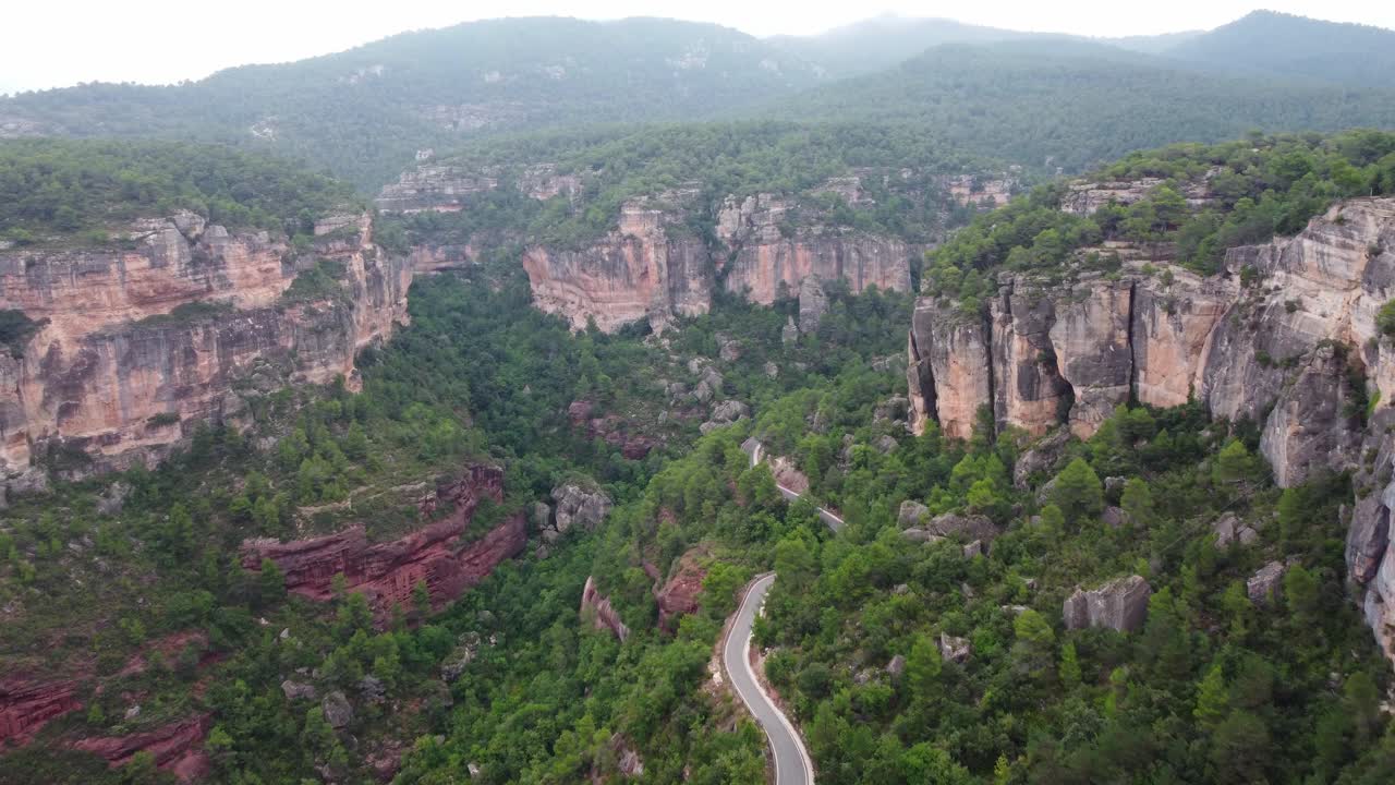 Siurana town nestled on cliffs in tarragona, lush greenery surrounding, winding road below, aerial view