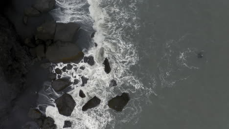 aerial: top down orbit shot of waves crushing on rocks in reynishjara black sand beach in iceland