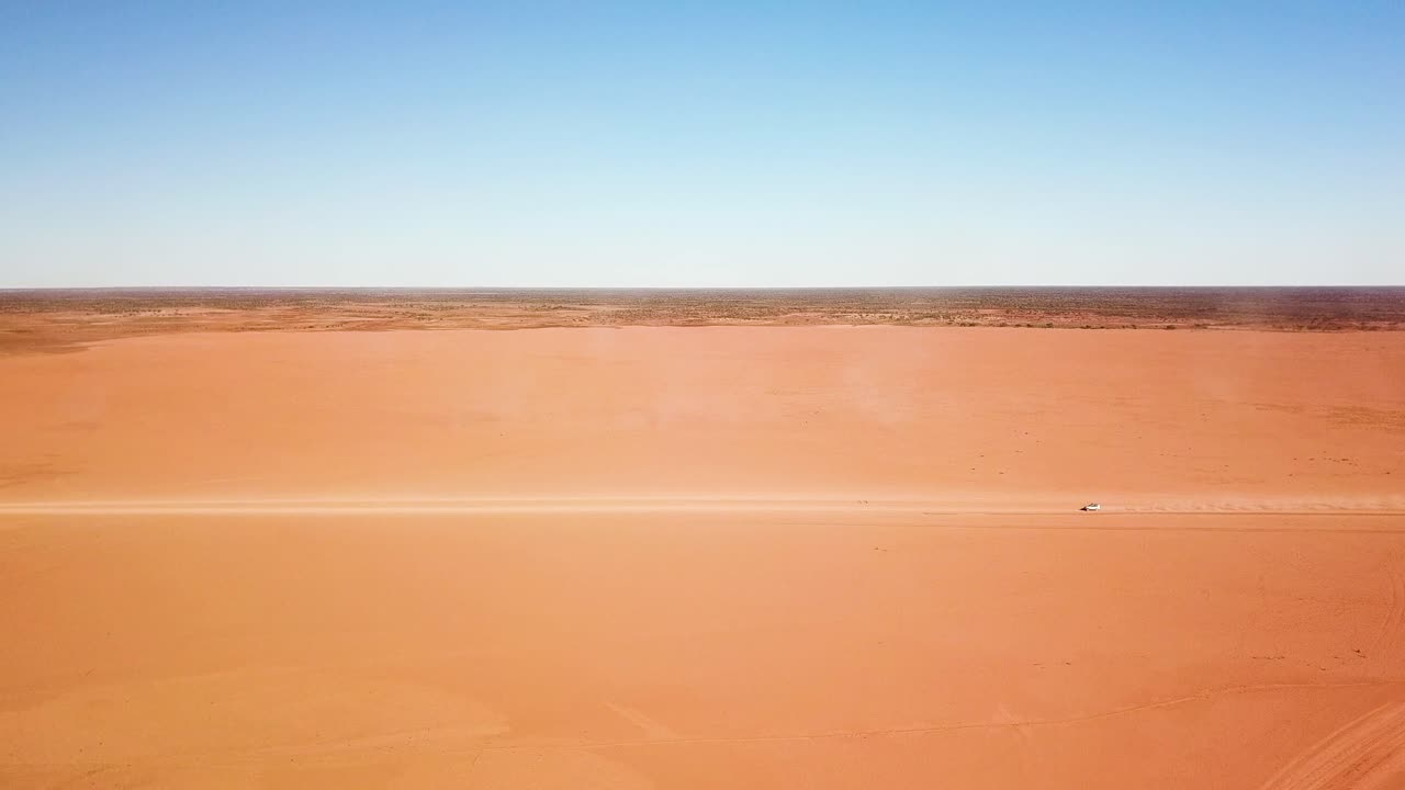 광대하고 황량하고 평평한 흙 지역을 가로질러 과속하는 자동차의 정지된 측면 항공 샷으로 큰 먼지 흔적을 남깁니다.