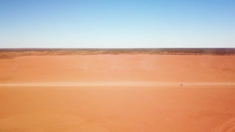 Stationary-side-on-aerial-shot-of-car-speeding-across-expansive,-desolate,-flat-dirt-area-leaving-large-dust-trail