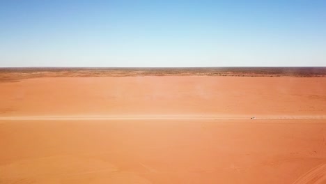 toma aérea lateral estacionaria de un automóvil a toda velocidad a través de un área de tierra plana, desolada y expansiva que deja un gran rastro de polvo