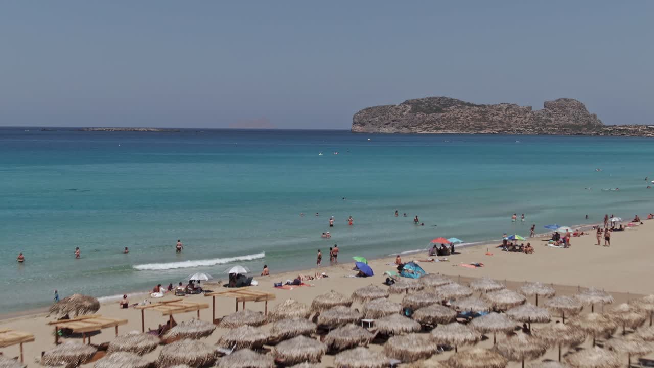 Flag of Greece wawing sandy coast of Falasarna beach in Crete island, drone ascend view