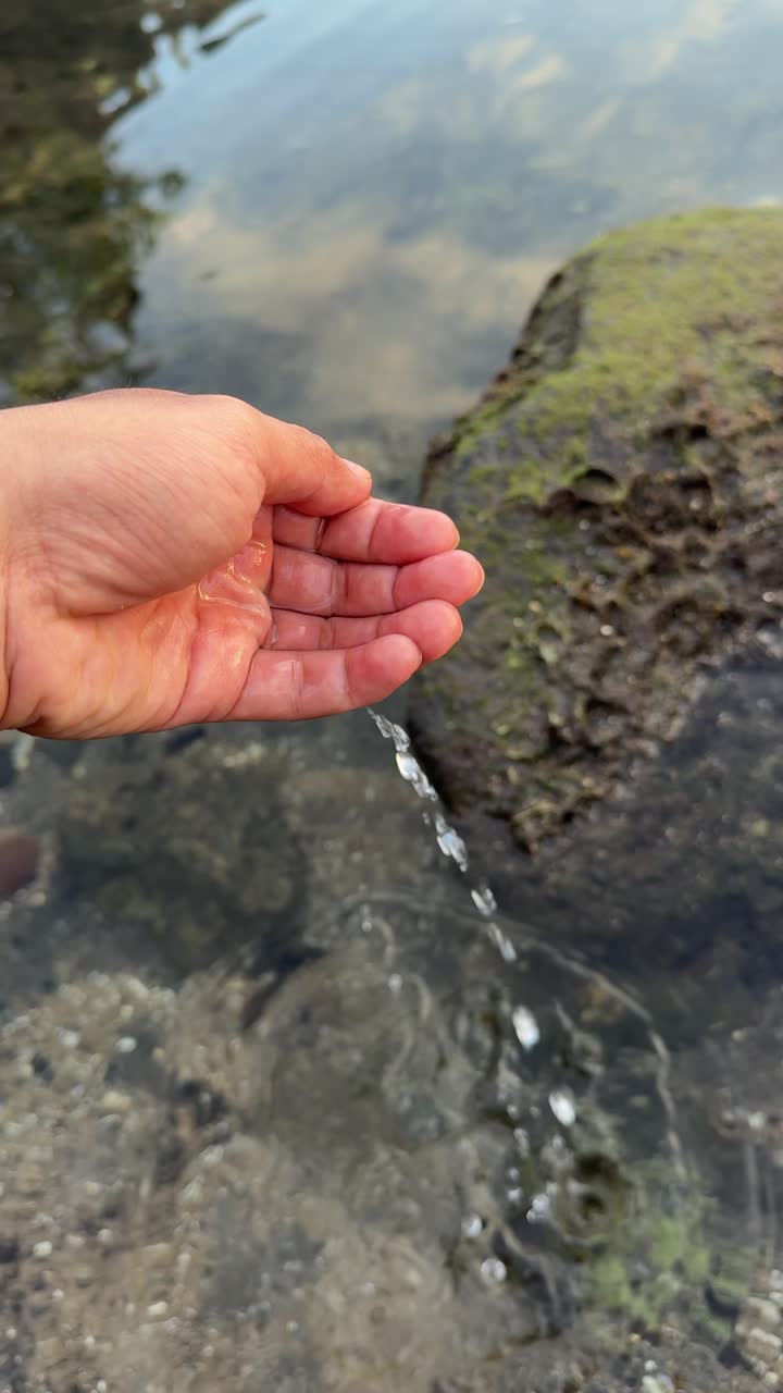Mano recogiendo y soltando agua clara de un estanque poco profundo
