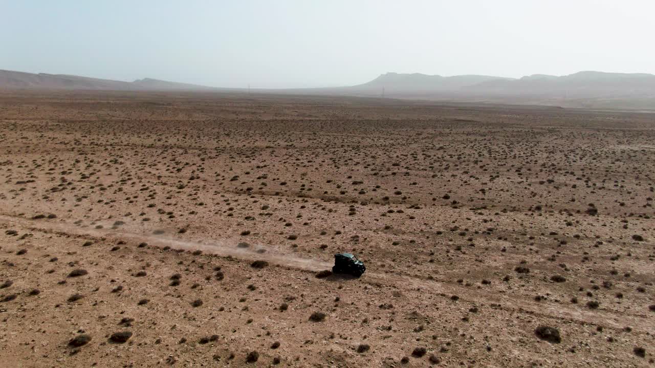 Ampia ripresa aerea con drone di un singolo fuoristrada che attraversa una pianura arida sconfinata, che evidenzia la scala, l'isolamento e l'immensità del paesaggio naturale circostante