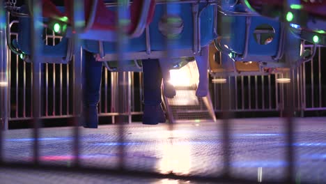 Father-and-daughter-legs-waiting-on-a-colorful-carousel-swing-seats-at-night-in-a-park