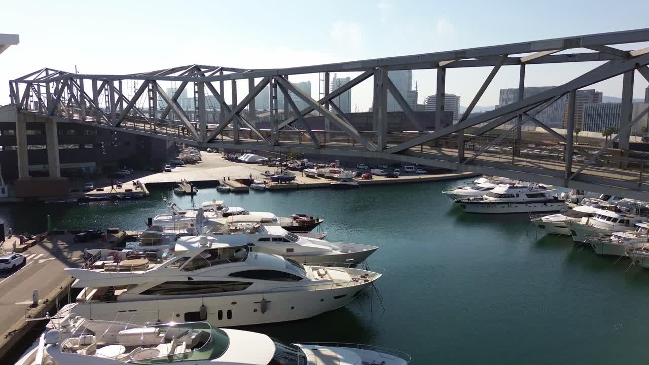 Toma aérea de yates de lujo descansando en el puerto de Barcelona con vistas de la ciudad al fondo