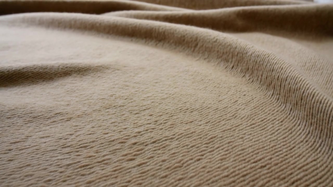 Primo piano della texture di una coperta di lana beige, morbide increspature e fibre sottili che catturano una calda luce laterale, atmosfera accogliente Hygge
