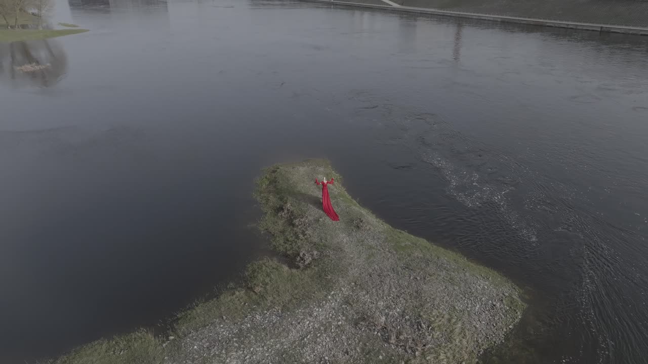 una vista dramática de avión no tripulado de modelo en vestido rojo caminando en una pequeña isla cerca de la ciudad