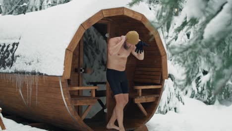 caucasian man come out of sauna and enter the barrel with frozen water.