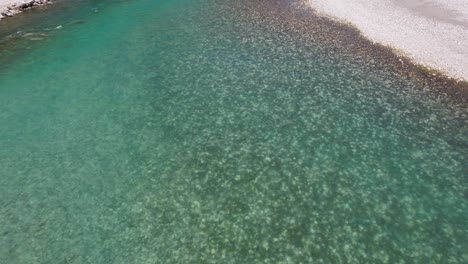 Emerald-river-with-water-streaming-over-pebbles,-liquid-texture-of-riverbed