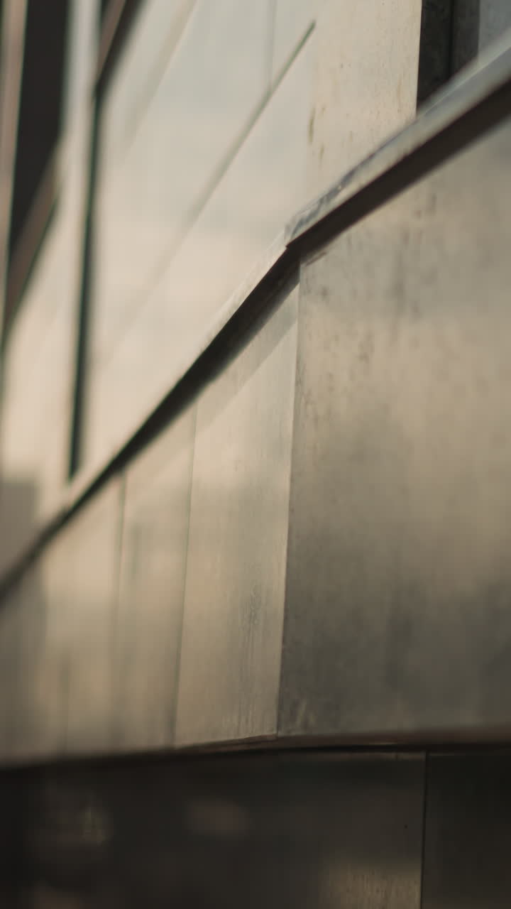 close de fachada de metal ao entardecer, ambiente urbano cinematográfico com painéis reflexivos e brilho suave do pôr do sol, profundidade de campo rasa e texturas discretas, trabalhador da manutenção inspecionando a costura, arquiteto estudando geometria, drone