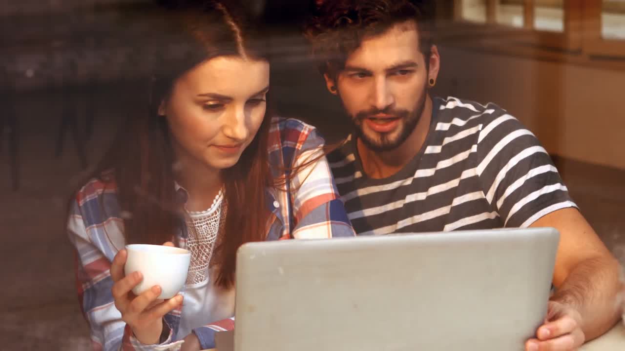 pareja feliz usando una computadora portátil mientras toman café