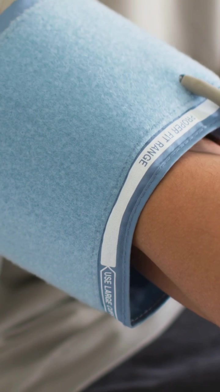 Vertical video: Adjusting hand with black bead band fitting blue cuff on arm on bed as check begins