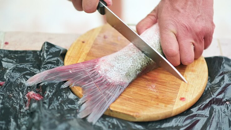 Primo piano di un uomo che taglia la coda di un pesce su un tagliere di legno