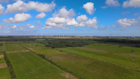 Aerial-truck-shot-over-agricultural-fields-on-summer-day-with-wind-turbine-farm