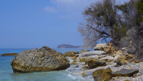 girl walking on rocky beach splashed by sea waves on beautiful seascape in ionian coastline
