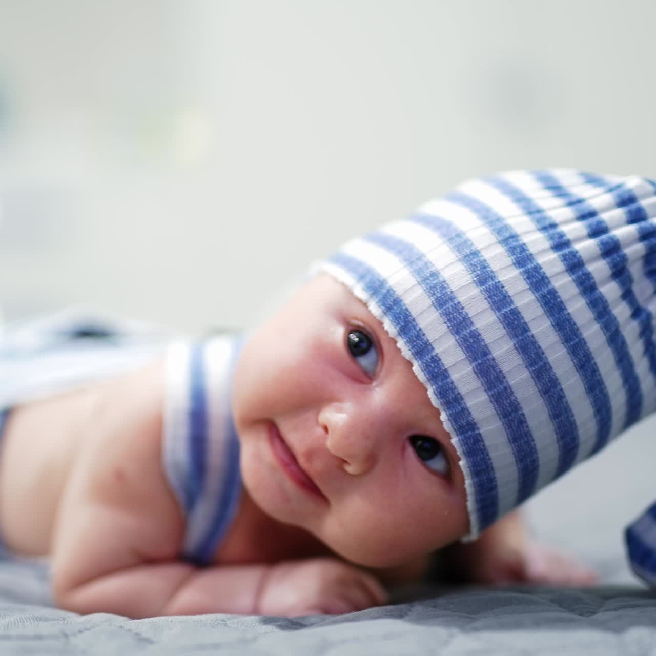 Sweet kid in funny striped suit lies on his belly. Lovely boy trying to keep his head up. Close up