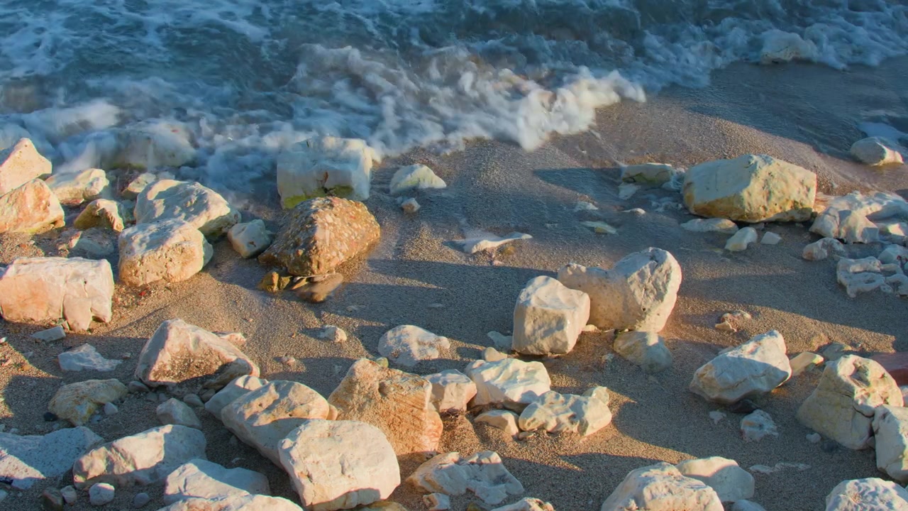 Onde marine al tramonto su rocce bianche, ripresa statica con treppiede. Dettaglio ravvicinato dell'acqua dell'oceano che si infrange su grandi pietre su una spiaggia sabbiosa durante l'ora d'oro