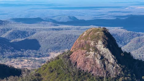 aerial drone footage pans smoothly across a rugged mountain peak in warrumbungle national park, revealing layered forested hills under clear morning light