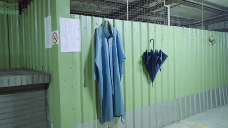 Purple-rain-coat-and-umbrella-hang-off-of-metal-hangar-on-green-corrugated-metal-fence