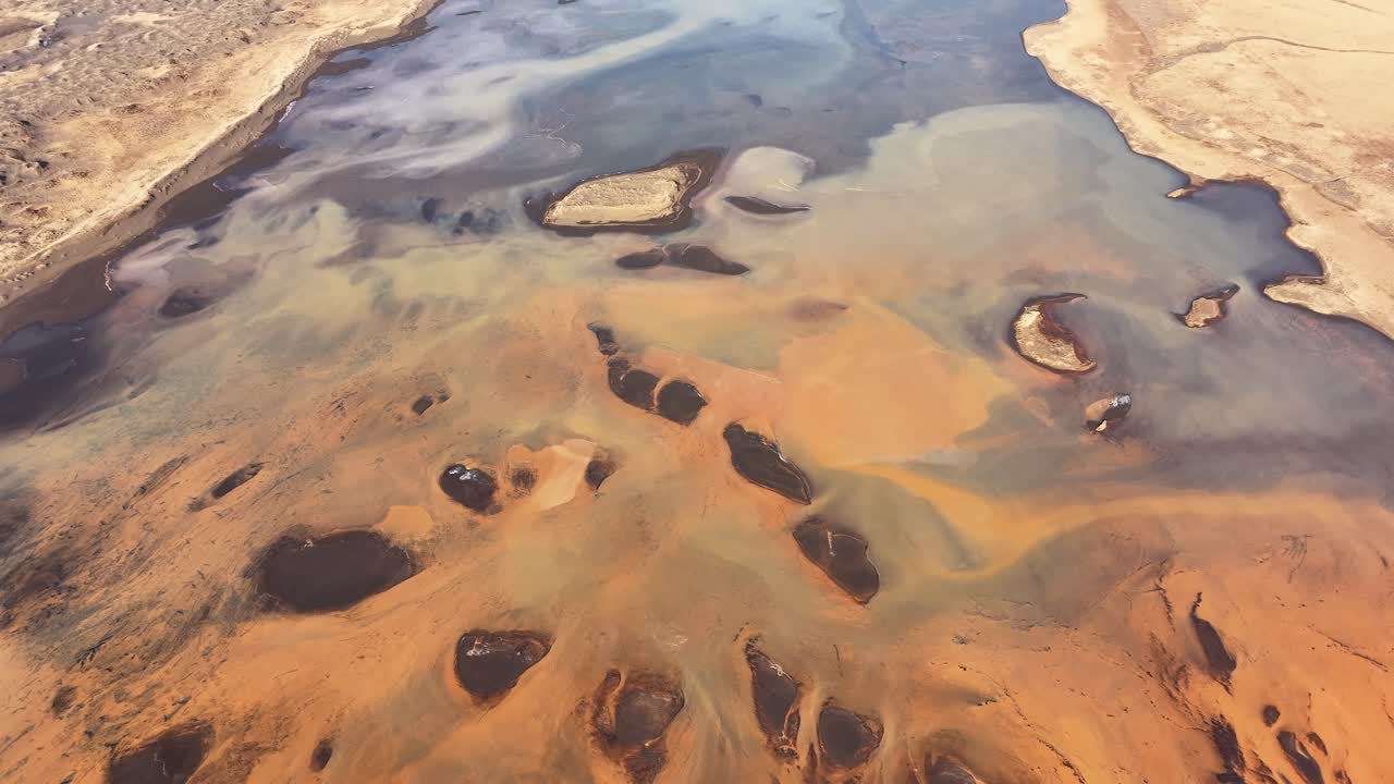 Aerial view of the Þjórsá River in Iceland, showing vibrant sediment patterns and scattered islets in a surreal, multicolored landscape.