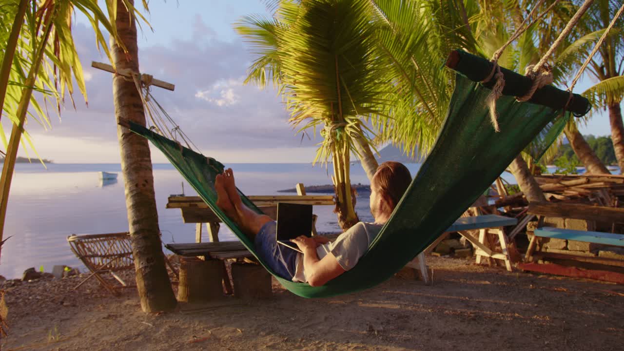 Man working with laptop relaxing on hammock on the beach. concept of digital nomad, remote worker, independent location entrepreneur