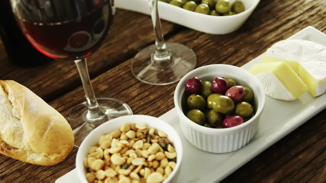 Coriandoli dorati che cadono e volteggiano attorno a pane, vino, olive e formaggio in un vassoio, per celebrare uno spuntino.