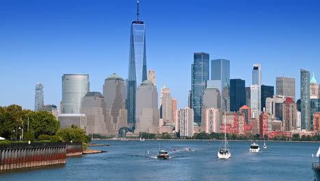 Diverse water vehicles on the Hudson River on sunny daytime. People walk by the riverside. View on Manhattan across the river from Jersey