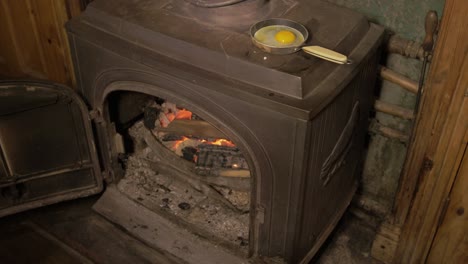 opening stove and filling with sticks to fry an egg