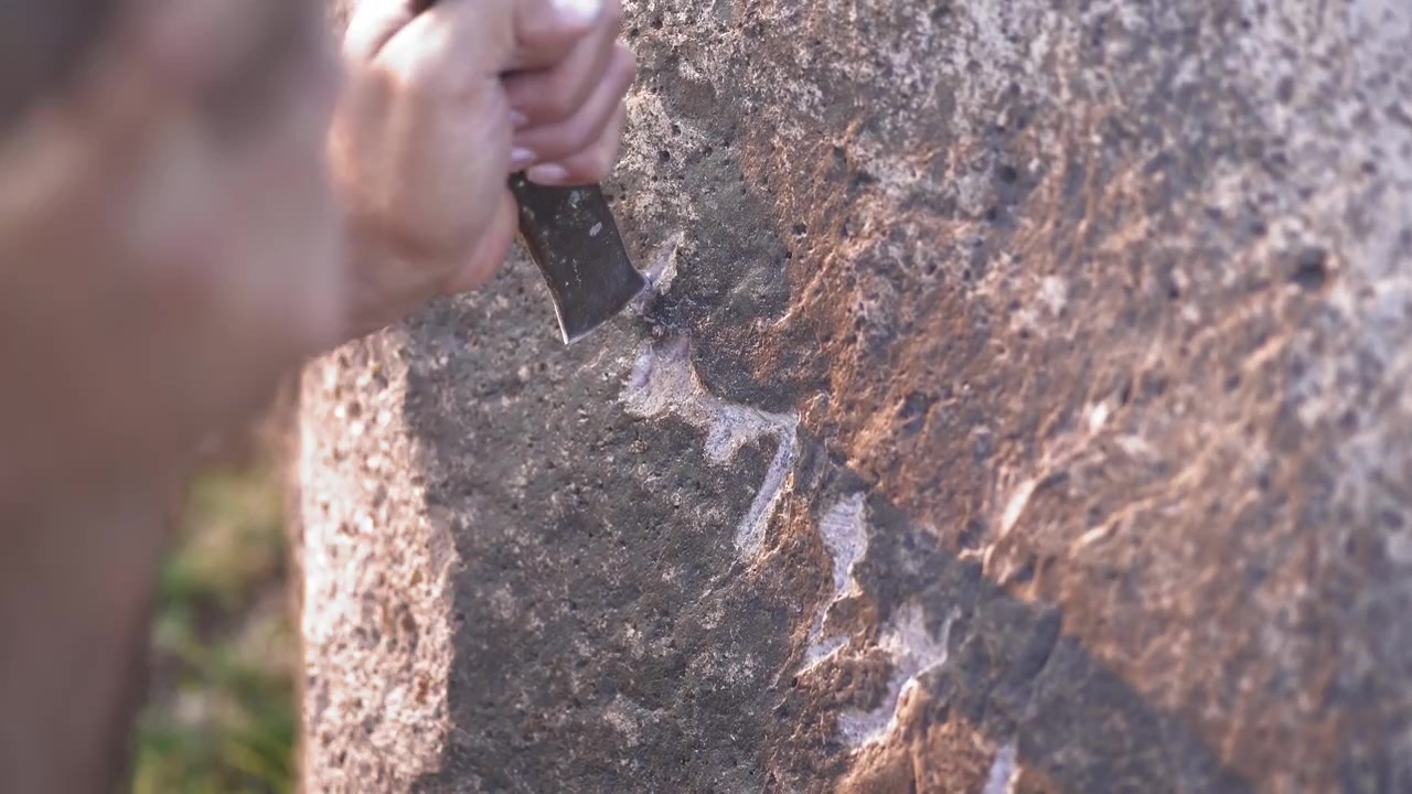 Person Carving Petroglyphs into a Large Rock Surface