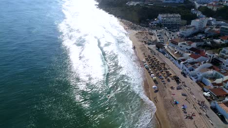 Luftaufnahme-Von-Wellen,-Die-Am-Schönen-Strand-Vor-Einem-Kleinen-Fischerdorf-Zusammenbrechen