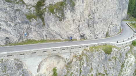 aerial of an male cyclist with blue jacket climbing the road on italian dolomites and waving to the camera