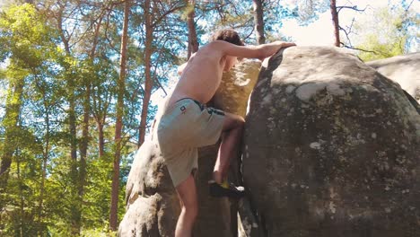 shirtless boy topping a boulder in pine forrest fontainebleau sun flares