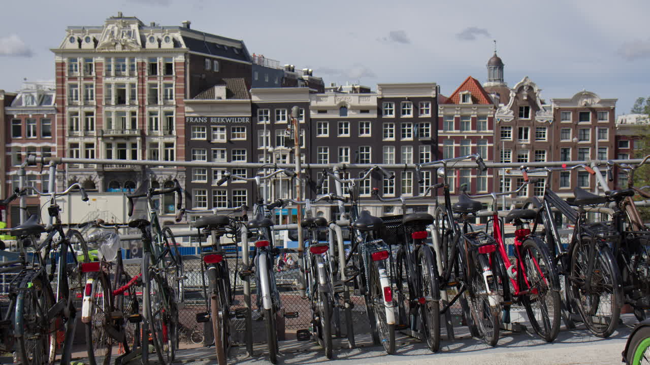 Bicycles Parked Along The Canal With Buildings In The Background In Amsterdam, Netherlands. Wide shot