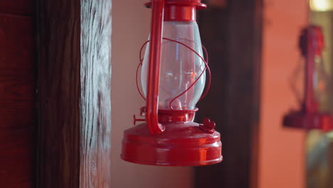 vista de cerca de una linterna roja de época colgando de una viga de madera con un fondo rústico, la estructura de vidrio y metal de la linterna está resaltada