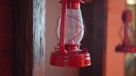 close-up view of a vintage red lantern hanging on a wooden beam with a rustic background, the lantern's glass and metal structure are highlighted