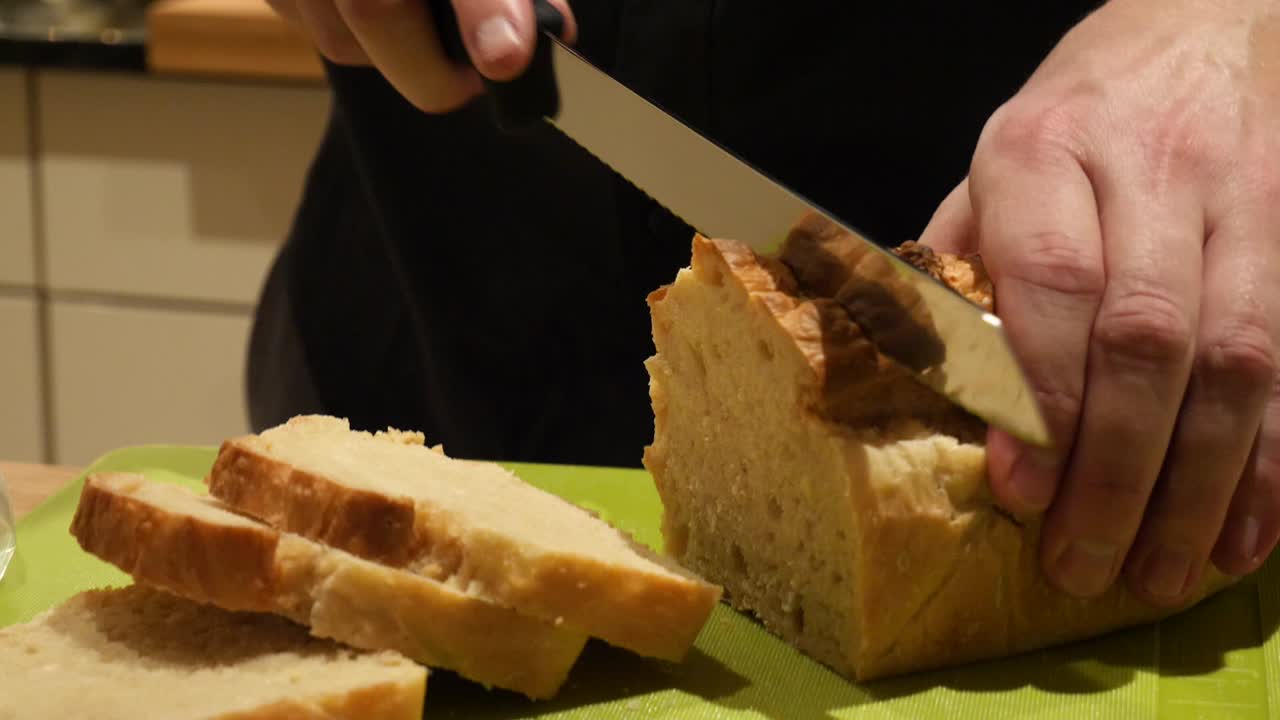 A white male hand model is slicing fresh baked toast bread on a green cutting board