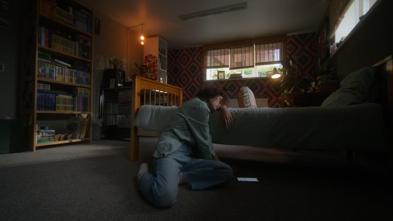 persona sentada en el suelo al lado de una cama en un dormitorio por la noche